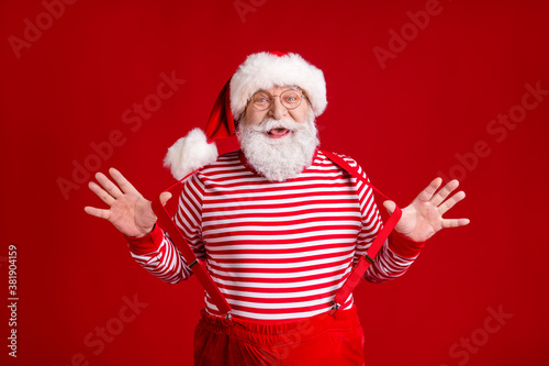 Photo of pensioner old man grey beard play straps funky entertain children newyear event wear santa costume suspenders spectacles striped shirt headwear isolated red color background © deagreez