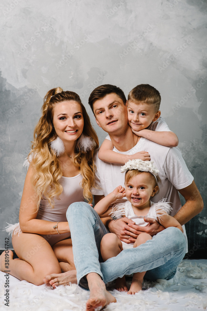 Happy family portrait in casual style clothes. Nice family wearing jeans isolated on grey wall. Smiling mother and father with daughter, son sitting on the floor. Fashion models plays with feathers.