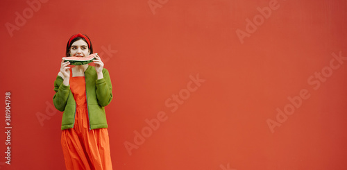 Long red banner. Young brunet girl eating watermelon Cool stylish red dress green jacket trendy clothes Funny mood fashion concept Bright emotional Horizontal composition Beautiful hair accessories  © Iryna&Maya