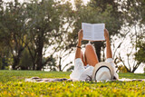 Young woman reads in the park.  Woman lying in the park reading a book  Woman with a white hat.  Concept of rest and pleasure.