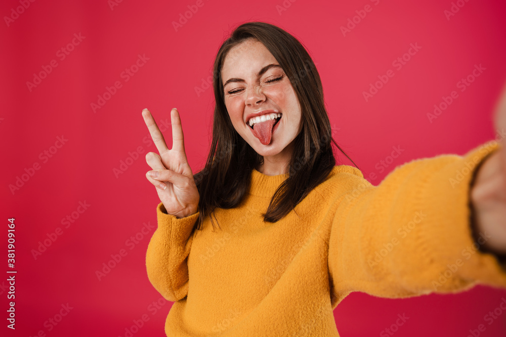 Image of joyful girl gesturing peace sign while taking selfie photo Image of joyful girl gesturing peace sign while taking selfie photo