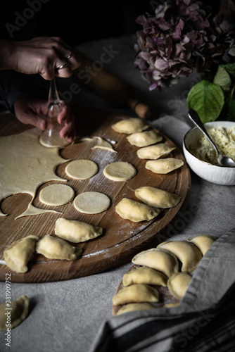 Step by step process of making Ukrainian pyrogy (Polish pierogi) with cottage cheese. Woman cutting dough rounds for pyrogy with glass.