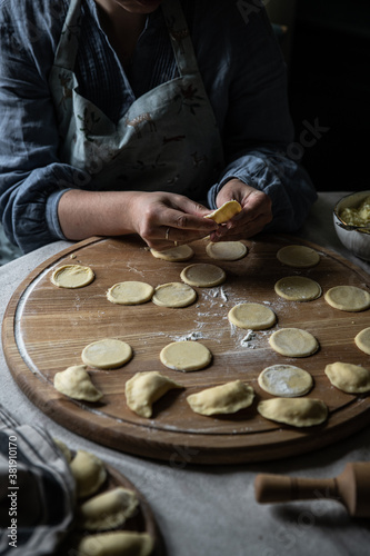 Step by step process of making Ukrainian pyrogy (Polish pierogi) with cottage cheese. Woman making pyrogy sitting by the table.