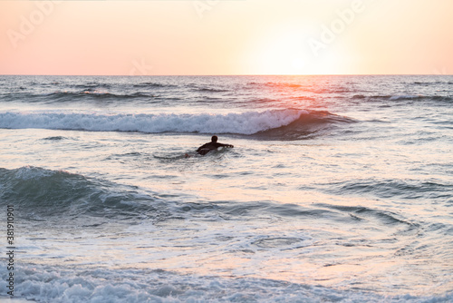surfer man swimming on the board entering the sea to surf at sunset
