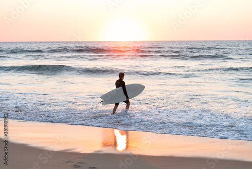 surfer man with the board in his arms entering the sea at sunset