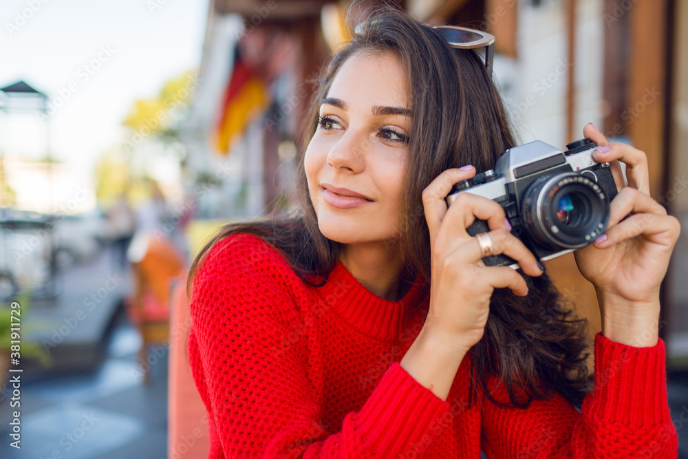 Inspired brunette woman having fun and  making photos on her vacations . Cold season. Wearing stylish red knitted sweater. City background.