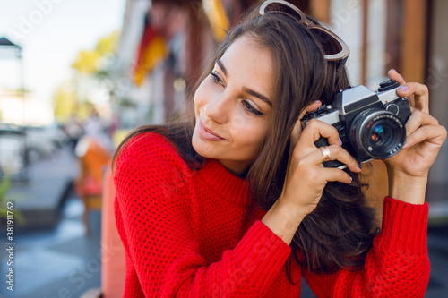 Inspired brunette woman having fun and making photos on her vacations . Cold season. Wearing stylish red knitted sweater. City background.