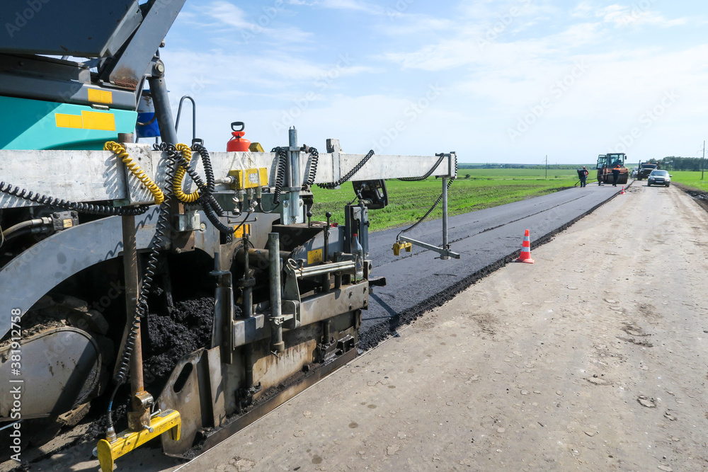 Paver machine on a new asphalt road surface. Road equipment on the construction site for road works. The asphalt surface. Workers and road construction machinery scenes.  Highway on a rural landscape