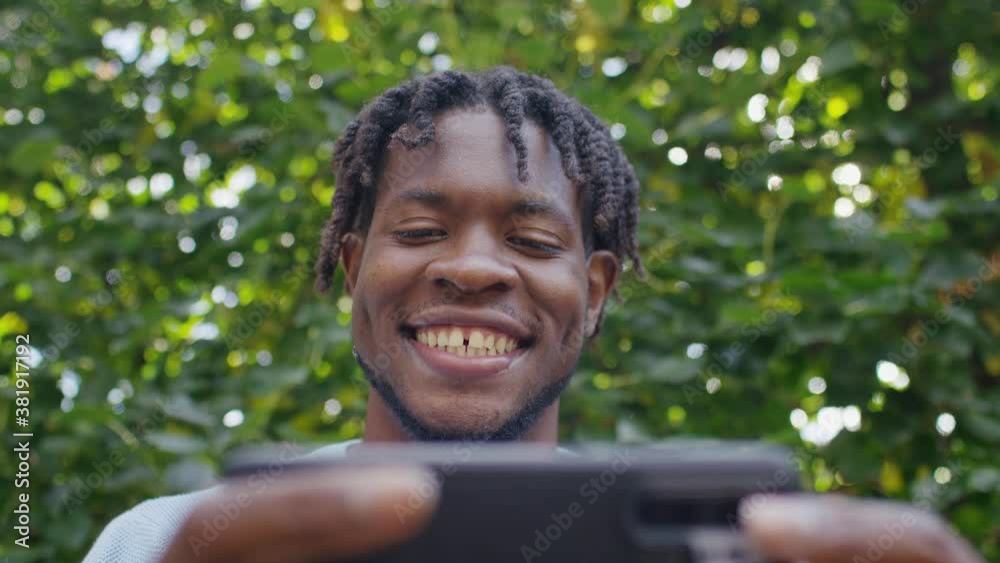 Young black male on his phone laughs as he watches something outdoors, in slow motion Young black male on his phone laughs as he watches something outdoors, in slow motion
