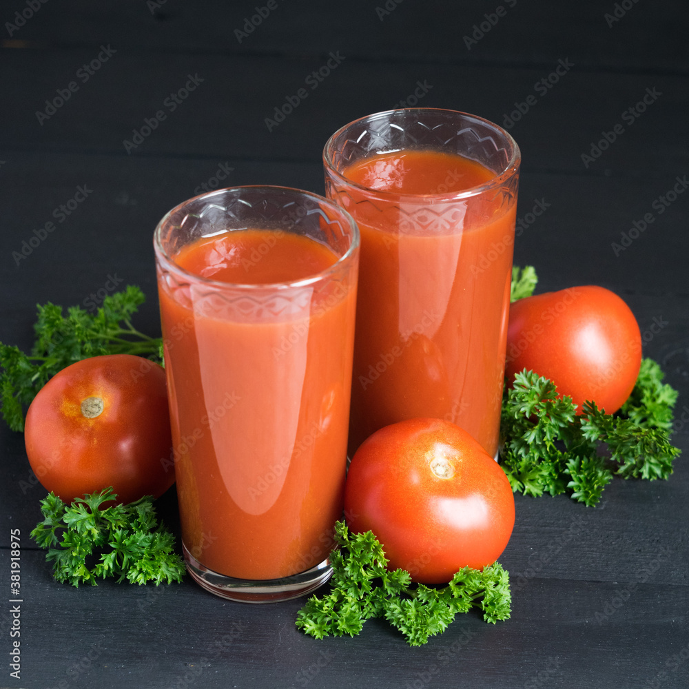 Two glasses of fresh tomato juice with red ripe tomatoes and parsley on black wooden background. Selective focus Two glasses of fresh tomato juice with red ripe tomatoes and parsley on black wooden background. Selective focus