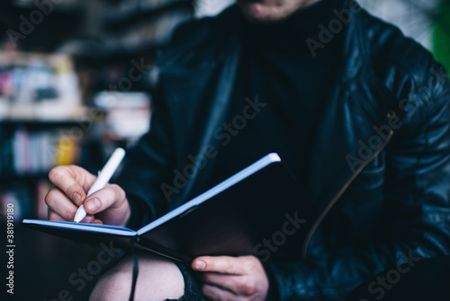 Crop freelancer writing in notebook in library