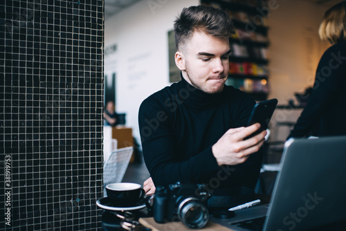Freelancer surfing internet on smartphone near laptop in cafe