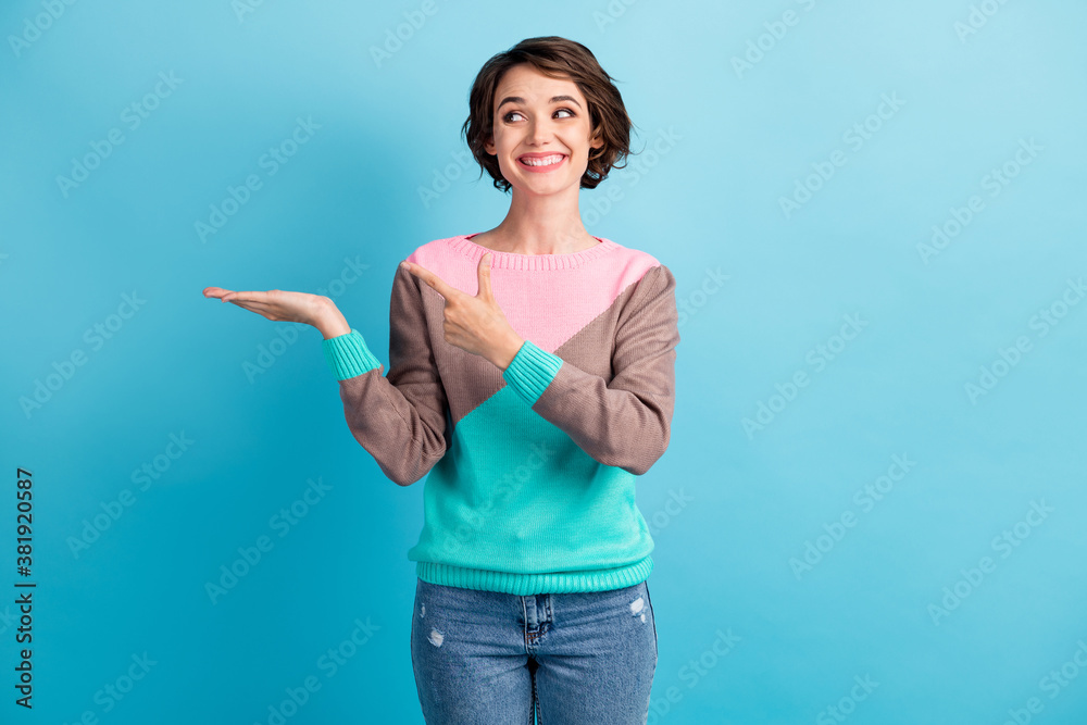 Photo portrait of happy smiling girl pointing finger demonstrating holding in hand blank space isolated on pastel light blue colored background
