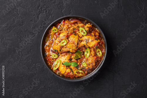 A Chicken Patiala in black bowl on dark slate table top. Murg Patiala is indian cuisine curry dish with chicken meat, spices, curd and cashew nut paste. Asian food and meal. Top view