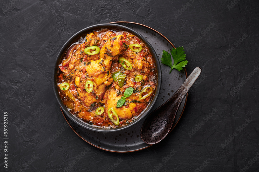 A Chicken Patiala in black bowl on dark slate table top. Murg Patiala is indian cuisine curry dish with chicken meat, spices, curd and cashew nut paste. Asian food and meal. Top view