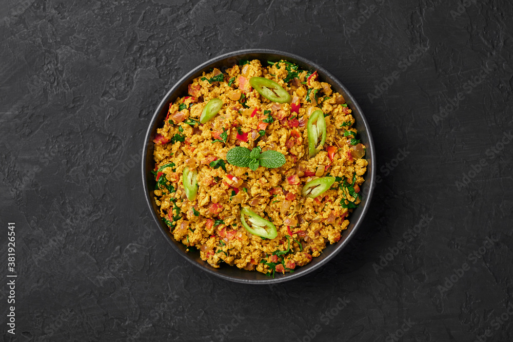 Masala Egg Bhurji or Muttai Podimas in black bowl on dark slate table top. Anda Bhurji is indian cuisine scrambled eggs dish with spices. Asian food and meal. Top view