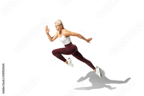 Running. Beautiful young female athlete practicing on white studio background  portrait with shadow. Sportive fit model in motion and action. Body building  healthy lifestyle  style concept.