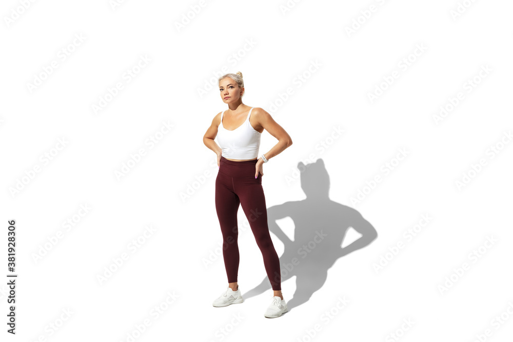 Posing. Beautiful young female athlete practicing on white studio background, portrait with shadow. Sportive fit model in motion, action. Body building, healthy lifestyle, style concept.