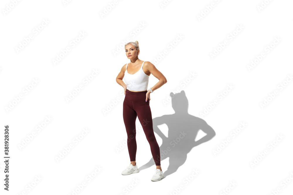 Obraz premium Posing. Beautiful young female athlete practicing on white studio background, portrait with shadow. Sportive fit model in motion, action. Body building, healthy lifestyle, style concept.