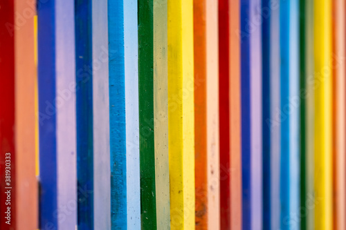Part of wooden, rainbow colorful painted fence on a sunny hot summer day in a city park. Abstract vivid multicolored background.
