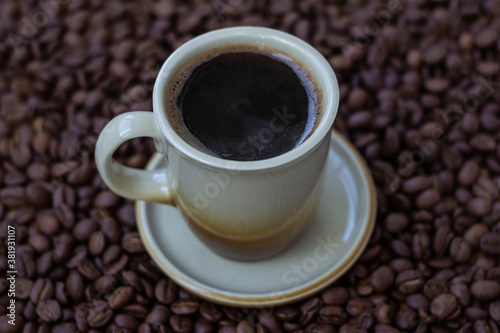 Black coffee in light brown cup on coffee beans background © Julia Snow