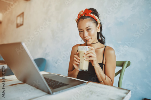 a young mixed race woman drink iced coffee and using her laptop in cafe