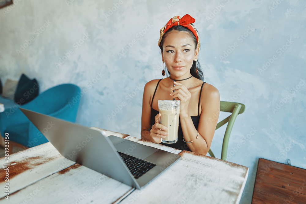a young mixed race woman drink iced coffee and using her laptop in cafe