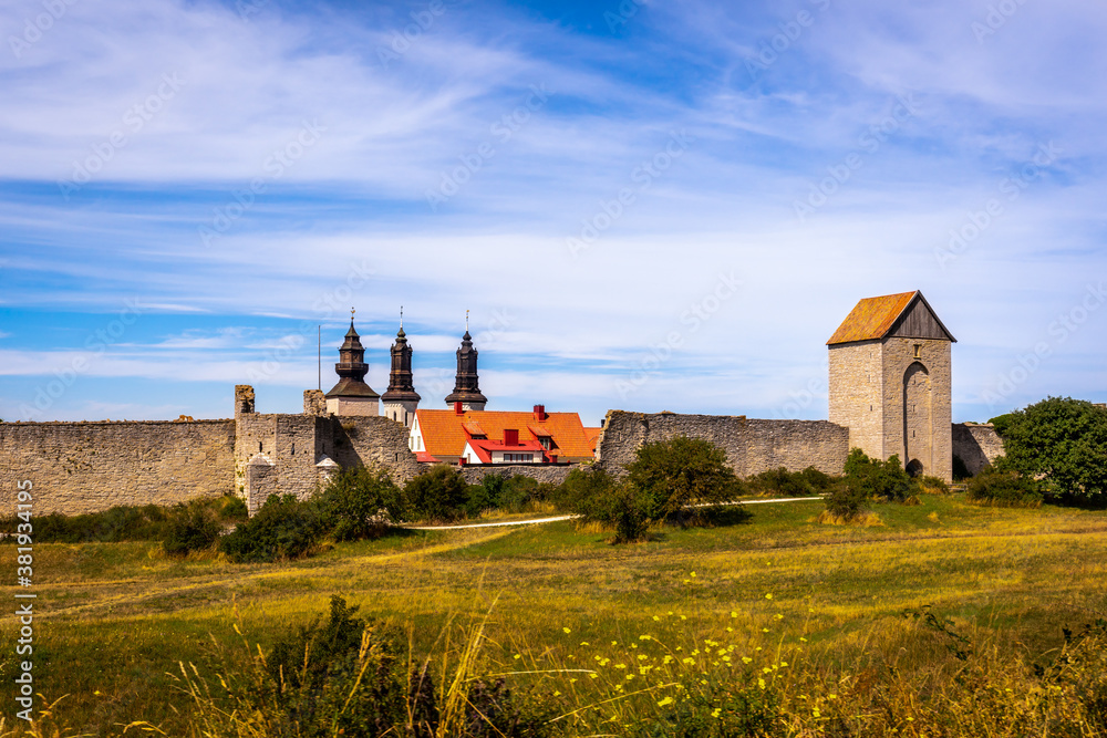 Beautiful rural summer view of an ancient medieval brick tower and defense wall surrounding the city of Visby Gotland, Sweden. Blue sky and grassy fields.