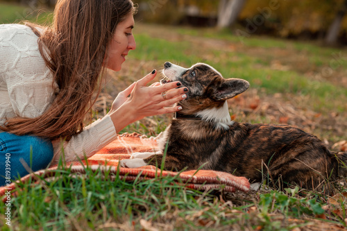 Happy woman together with Welsh Corgi dog in a park outdoors. Young female owner hugging pet in park on red blanket plaid. love and care for the pet. Back view