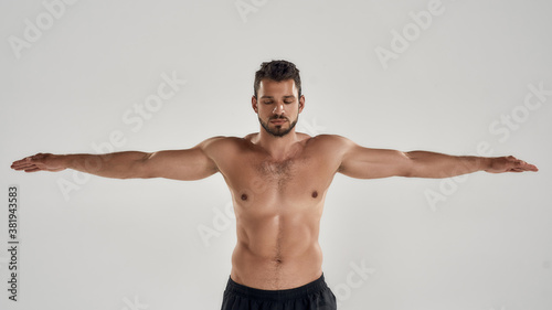 Ready to swim. Young athletic man with naked torso keeping eyes closed while posing with outstretched arms isolated over grey background