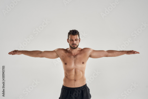 Swimming. Young athletic man with naked torso keeping eyes closed while posing with outstretched arms isolated over grey background