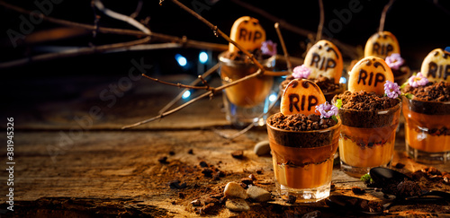 Graveyard chocolate mousse cups with tombstone cookies, copy space for text. Halloween dessert