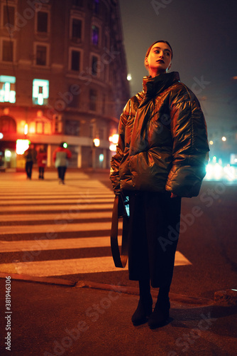 Stylish woman on crosswalk in yellow light at night