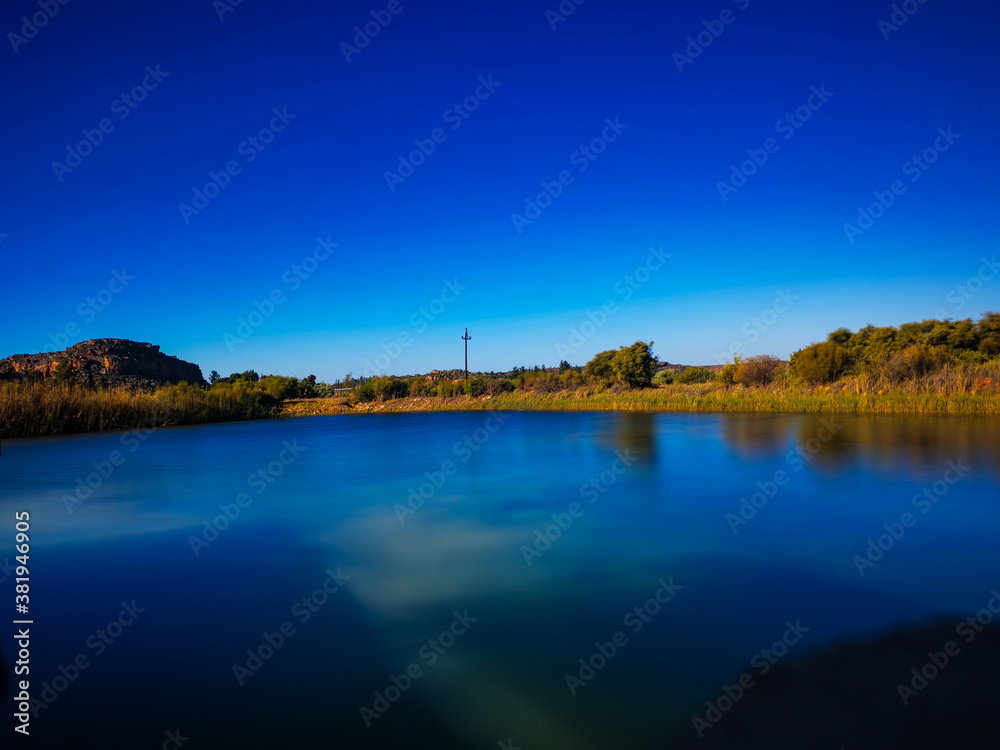Still Lake / Dam / River on farm with reflection, summer day, blue sky, powerlines, Alpha Excelsior Dam, Rocklands, Cederberg, South Africa 