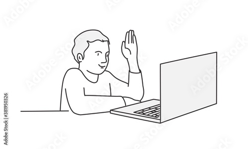 Student sitting at a table in front of a laptop with a raised hand.