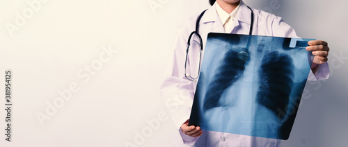 Middle aged of asian woman doctor standing and holding a x-ray film or radiography. she looking for unnormal or disease on lungs which illness from coronavirus pandemic. photo