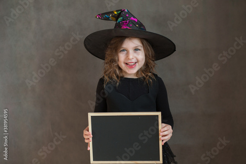 Happy girl in halloween witch costume with black desk in hands
