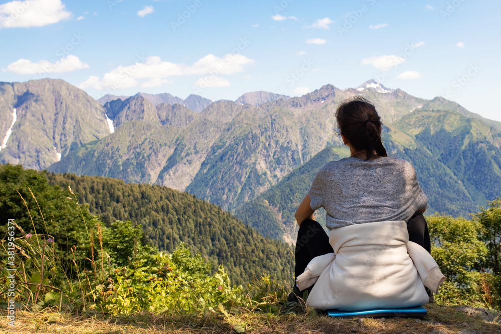 Fototapeta premium Travel, adventure and trekking by Hiking in the mountains. girl is sitting on a scenic peak, looking at the landscape