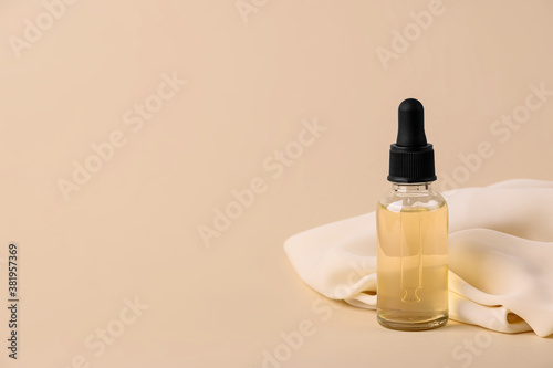 Glass bottle with a pipette with serum on a beige background with textiles. Silky texture of a beauty product for skin care. Women's cosmetics for face moisturizing with vitamins. Copy space