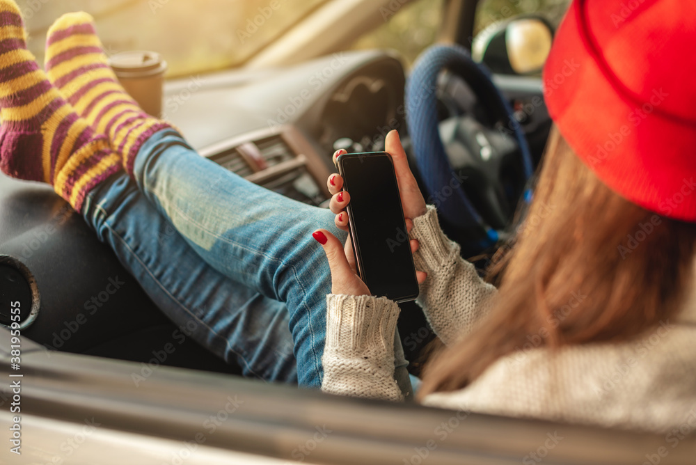 Φωτογραφία Woman in a car in warm socks is holding a mobile phone gadget at sunset