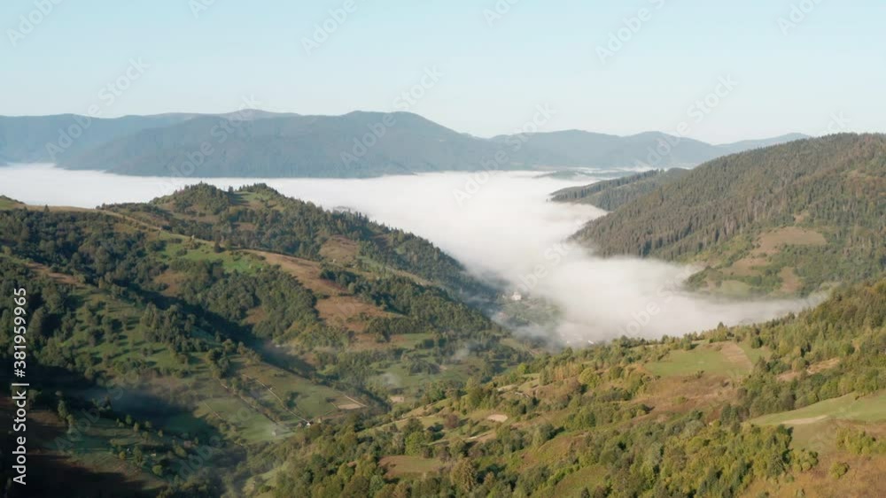 Aerial view. Mountain landscape. A valley covered with fog. Carpathians in the autumn morning. Wonderful natural background. Mountain slope with trees and view of the valley