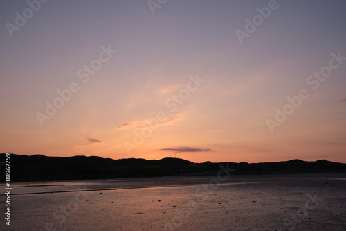 Sunset on Uisken beach in the Ross of Mull on the Isle of Mull  Scotland. Reflections of the colourful sunset are seen in the wet sand in the foreground and wind turbines are centre frame.