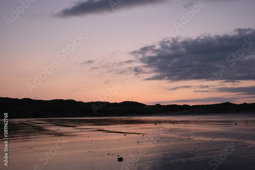 Sunset on Uisken beach in the Ross of Mull on the Isle of Mull  Scotland. Reflections of the colourful sunset are seen in the wet sand in the foreground and wind turbines are centre frame.