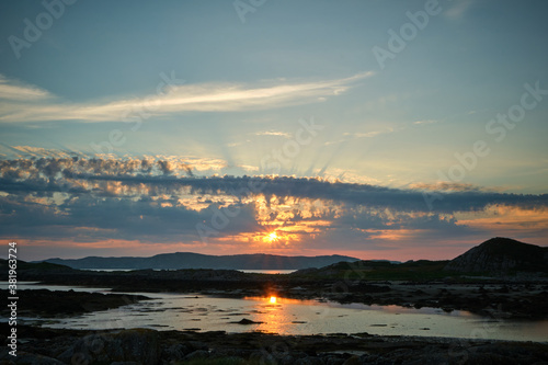 A dramatic sunset on Fidden Beach, Isle of Mull, Scotland. Impressive cloud formations fill the sky at different levels and the sun reflects in the water in the foreground.
