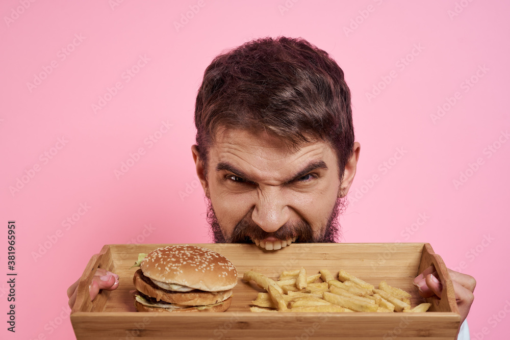Aggressive guy with a tray in his hands hamburger fries pink background hungry look Aggressive guy with a tray in his hands hamburger fries pink background hungry look