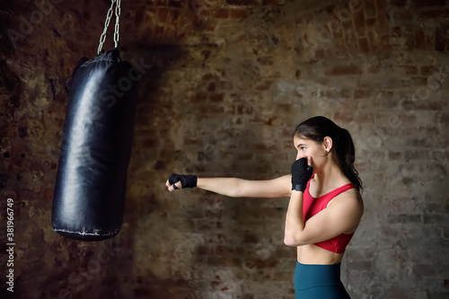 Young woman hits punching bag during a boxing training. Female boxer doing fitness.