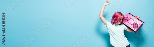 young woman with pink hair holding vintage tape recorder and dancing on blue background, panoramic shot photo