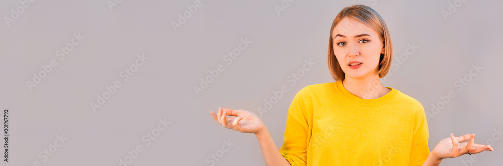 Portrait of a young woman shrugging shoulders over gray background Portrait of a young woman shrugging shoulders over gray background