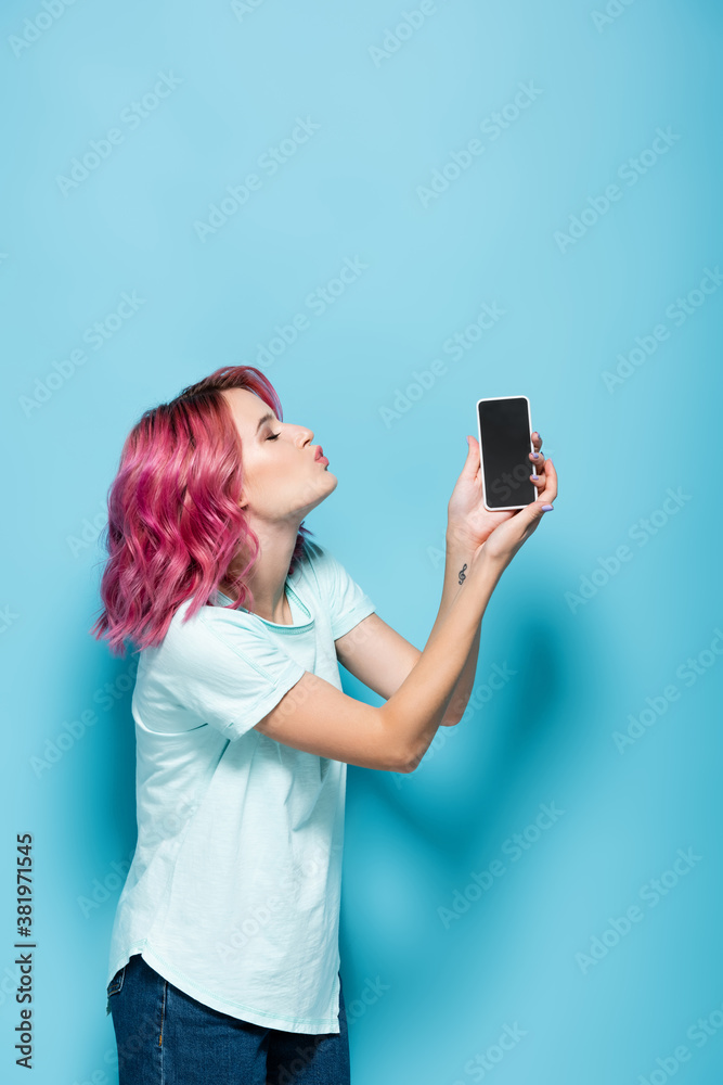 young woman with pink hair kissing smartphone with blank screen on blue background young woman with pink hair kissing smartphone with blank screen on blue background