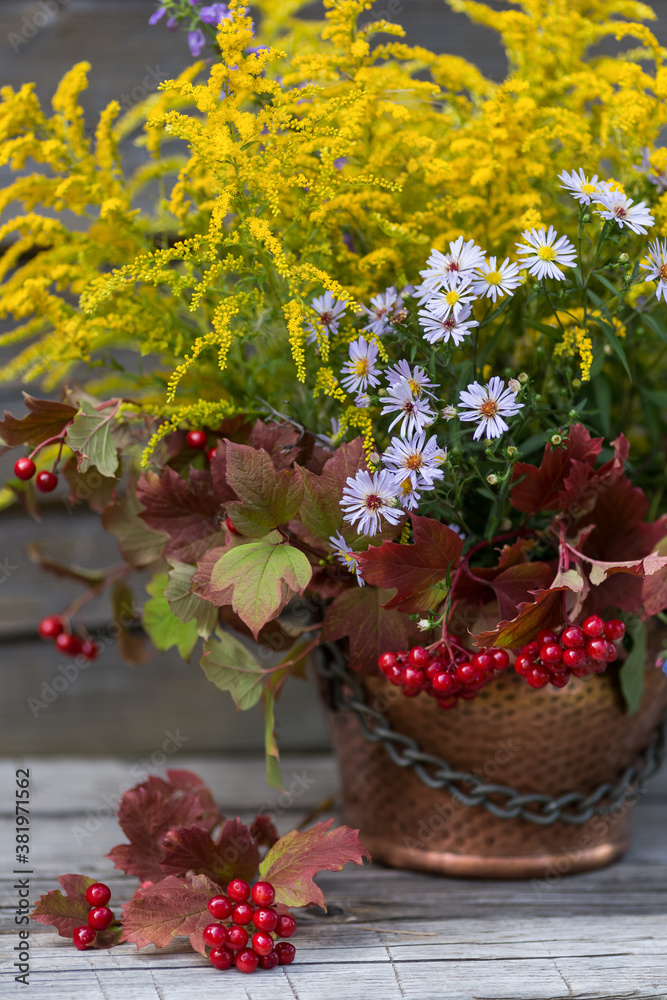 Autumn bouquet of flowers with viburnum berries in a copper planter outdoors
